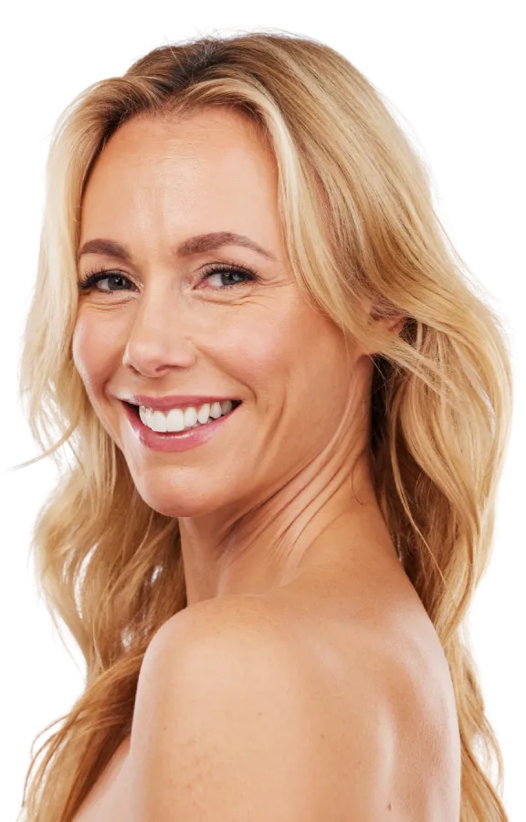 Portrait of a smiling blonde woman with wavy hair, shoulders visible, looking slightly over her shoulder with a friendly expression.