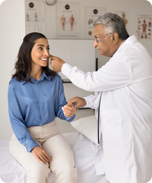 Doctor in a white coat examines a smiling woman during a medical checkup in a clinic, lifting her jaw near the ear.